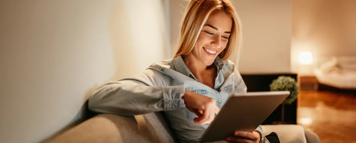 Frau sitzt auf einem Sofa und liest die digitale Zeitung auf einem Tablet